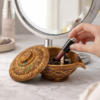 Person applying lipstick in front of a mirror with a decorative wooden container on a marble surface.
